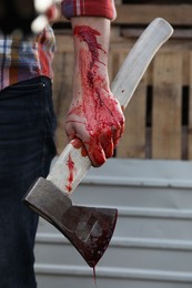Man holding bloody axe outdoors, closeup view