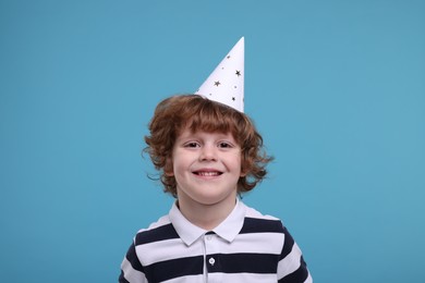 Photo of Happy little boy in party hat on light blue background
