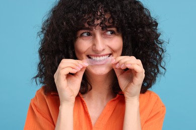 Photo of Young woman applying whitening strip on her teeth against light blue background