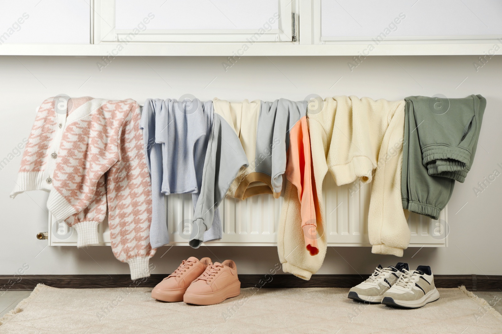 Photo of Heating radiator with clothes and shoes in room