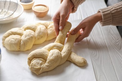 Photo of Woman cooking braided bread at white wooden table in kitchen, closeup. Traditional Shabbat challah