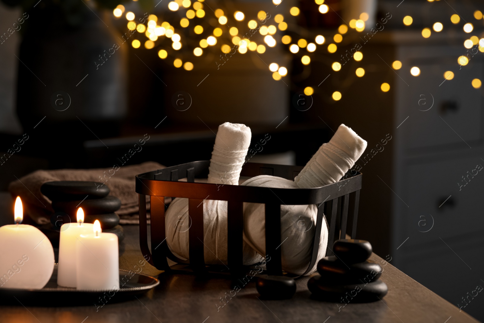 Photo of Herbal massage bags, burning candles and stones on grey table. Spa products