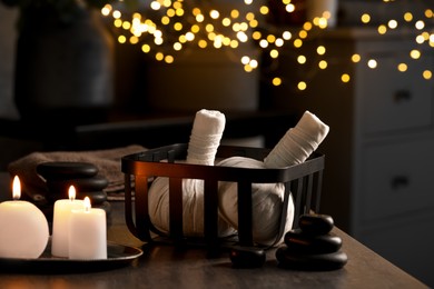 Photo of Herbal massage bags, burning candles and stones on grey table. Spa products