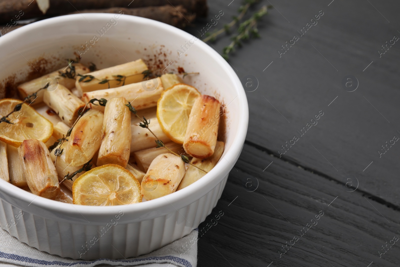 Photo of Dish with baked salsify roots, lemon and thyme on black wooden table., closeup Space for text