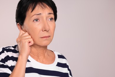 Senior woman suffering from ear pain on light grey background, closeup. Space for text