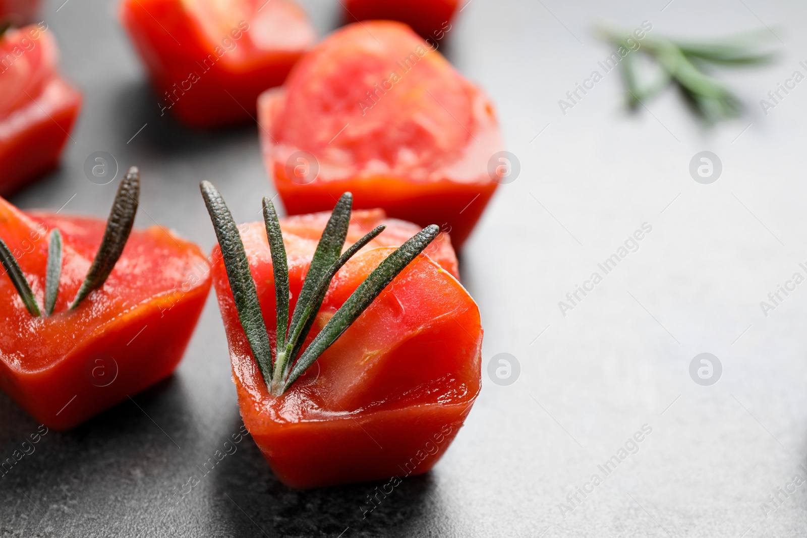 Photo of Ice cubes with tomatoes and rosemary on grey table, closeup