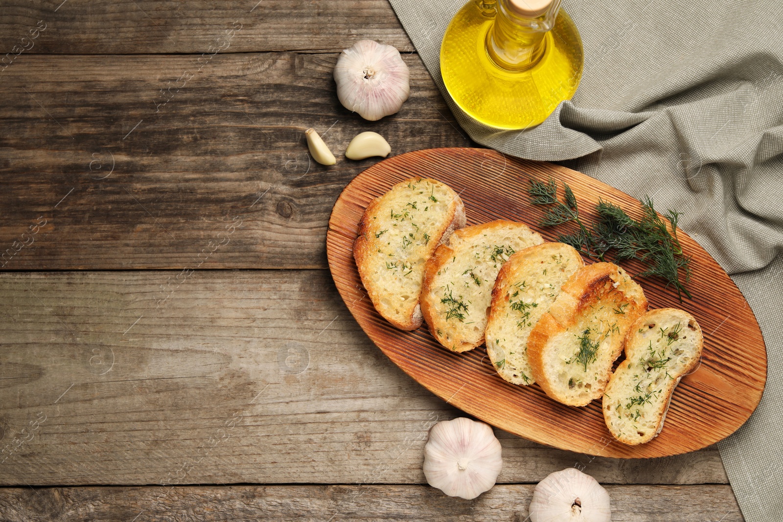 Photo of Tasty baguette with garlic, dill and oil on wooden table, flat lay. Space for text