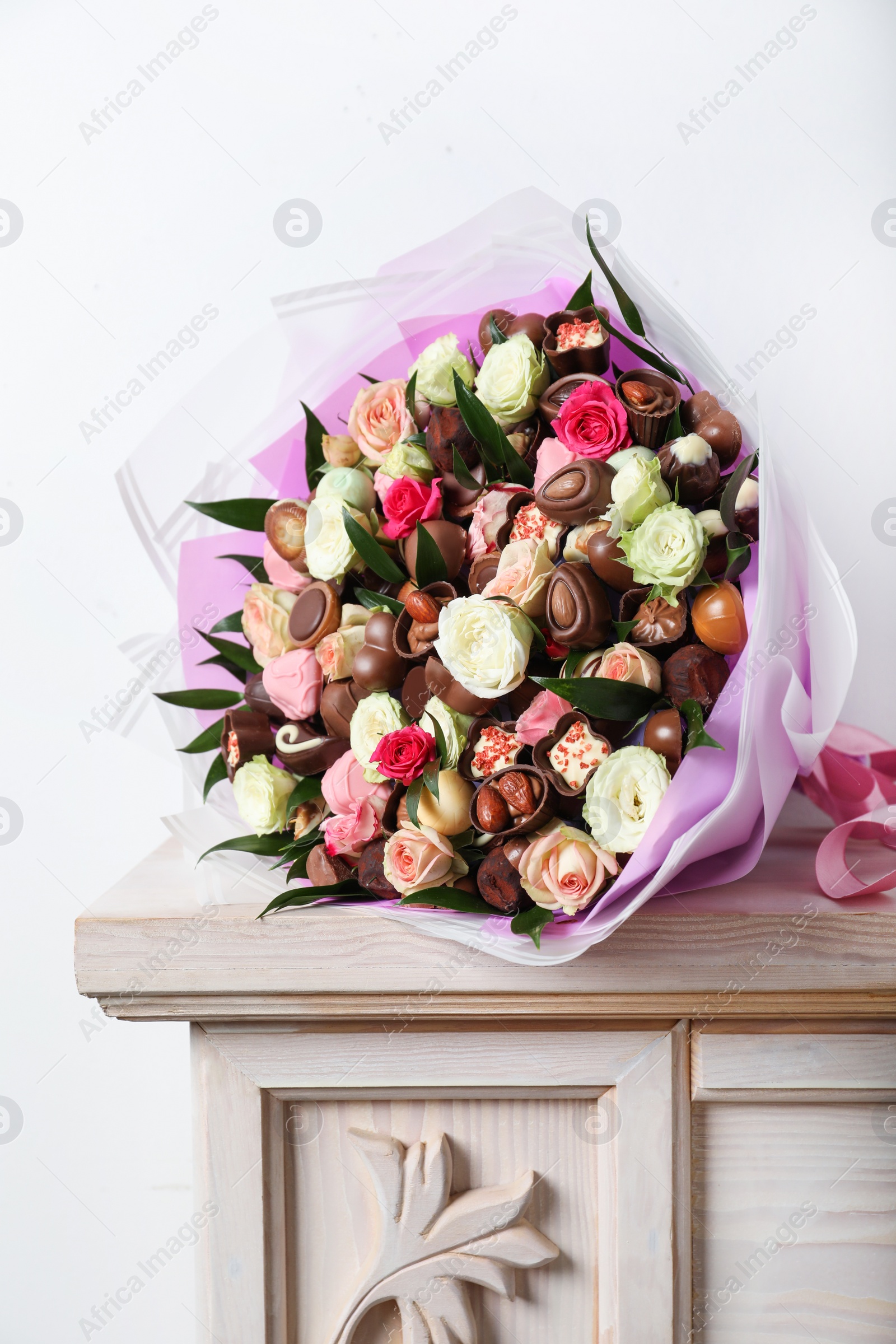 Photo of Beautiful bouquet of flowers and chocolate candies on wooden shelf against white background