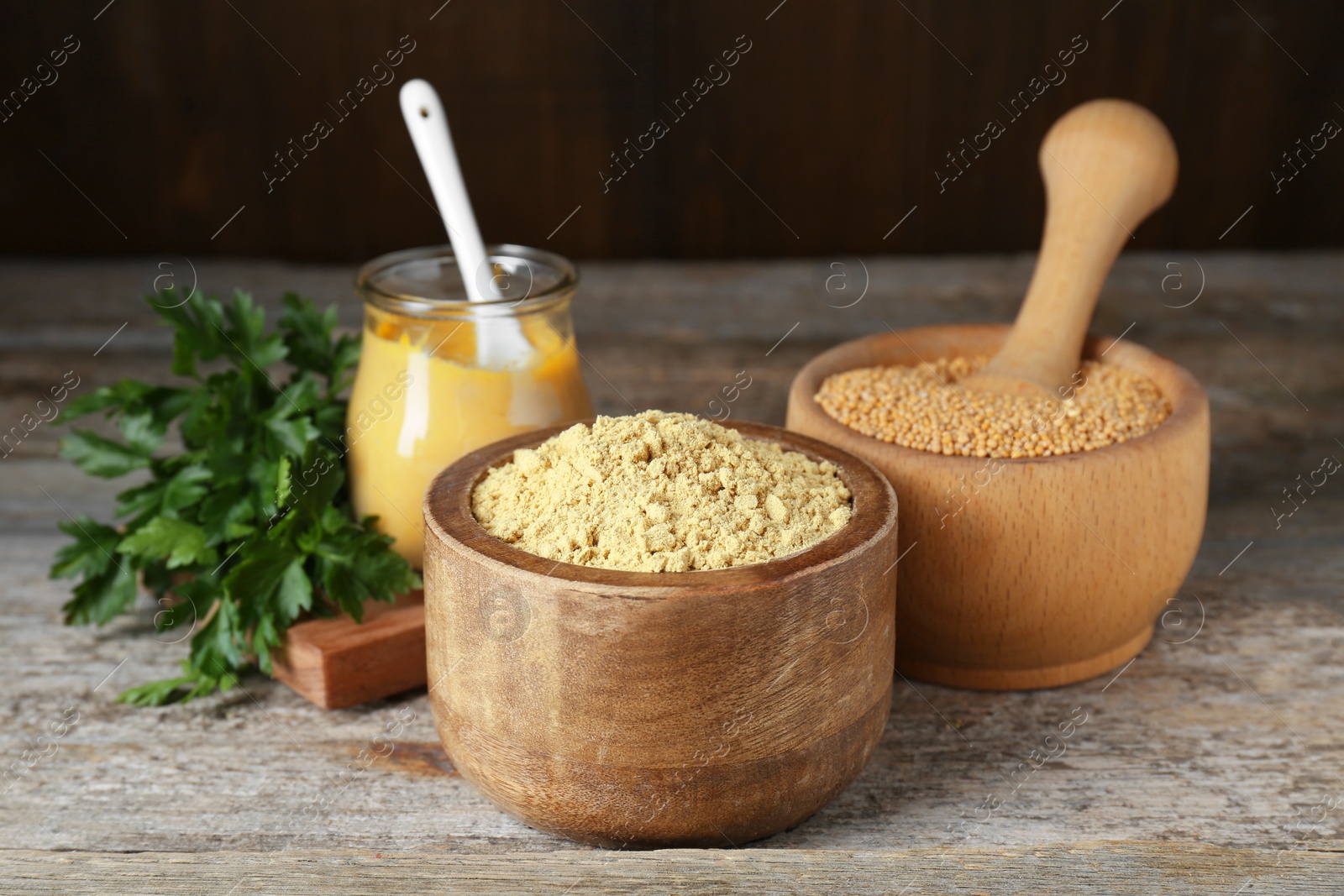 Photo of Bowl of mustard powder, parsley and mortar with seeds on wooden table