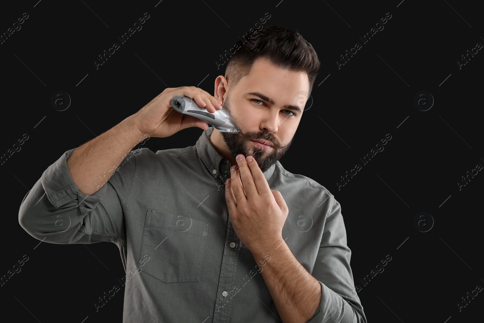 Photo of Handsome young man trimming beard on black background