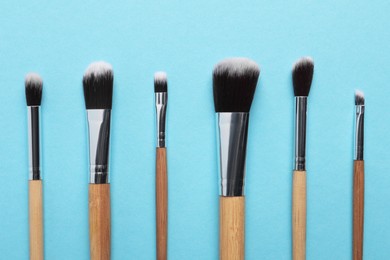 Different makeup brushes on light blue background, flat lay