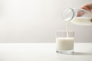 Woman pouring milk into glass at white table, closeup. Space for text