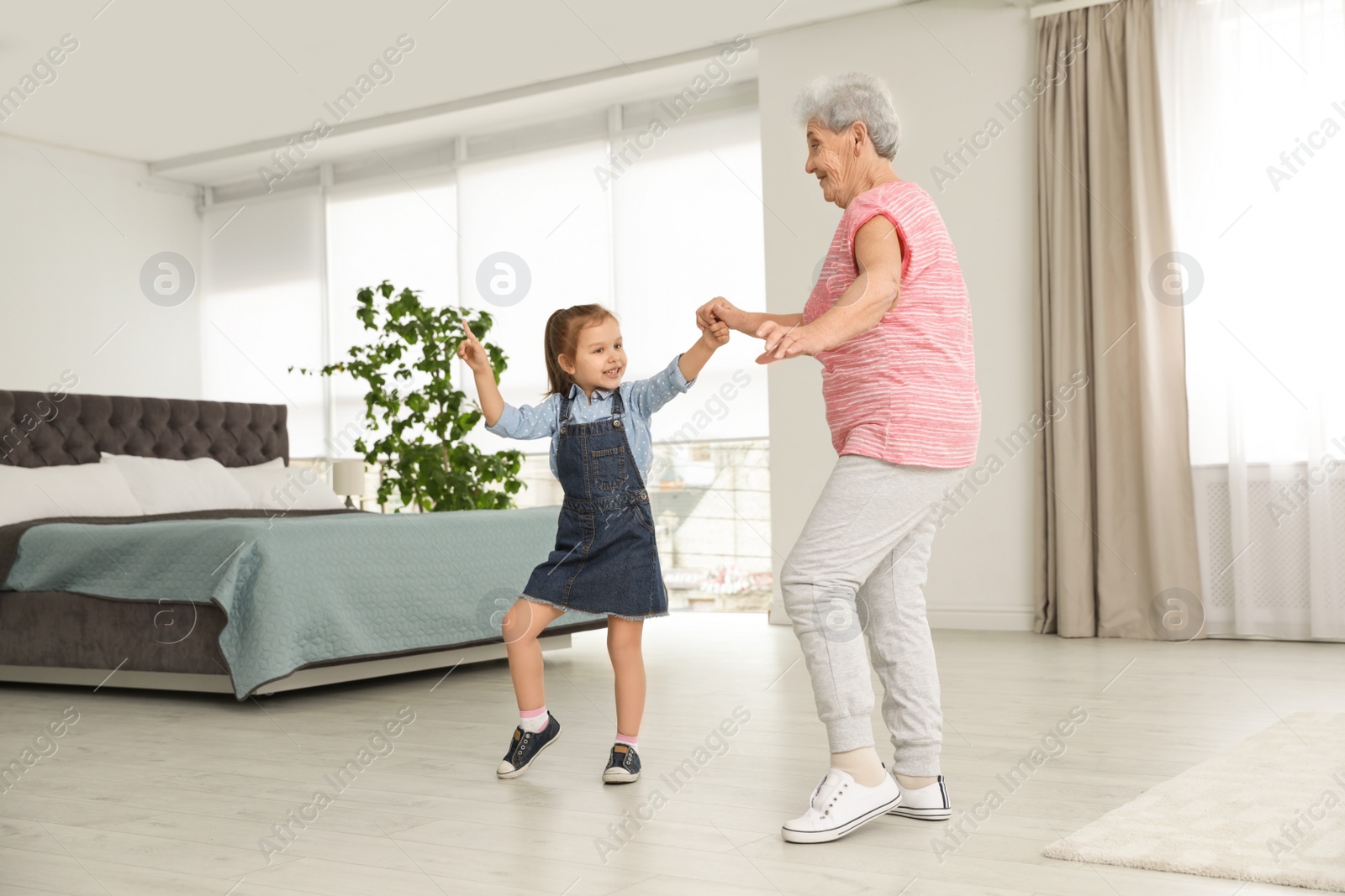 Photo of Cute girl and her grandmother dancing at home