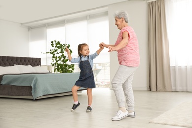 Cute girl and her grandmother dancing at home