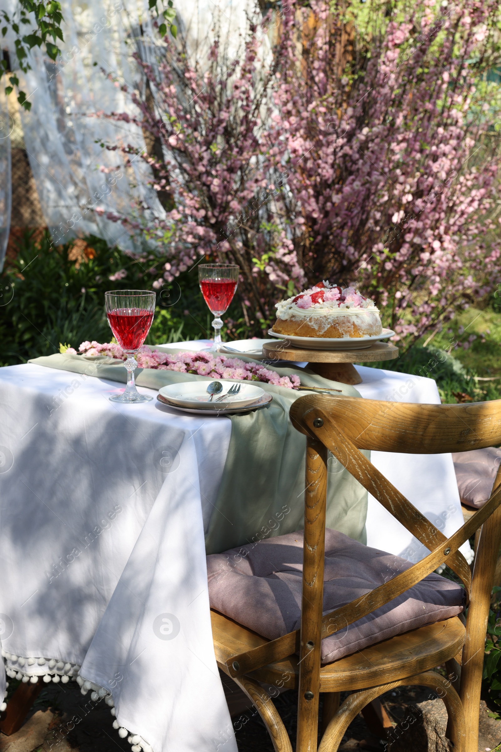 Photo of Beautiful spring flowers, delicious cake and wine glasses on table in garden