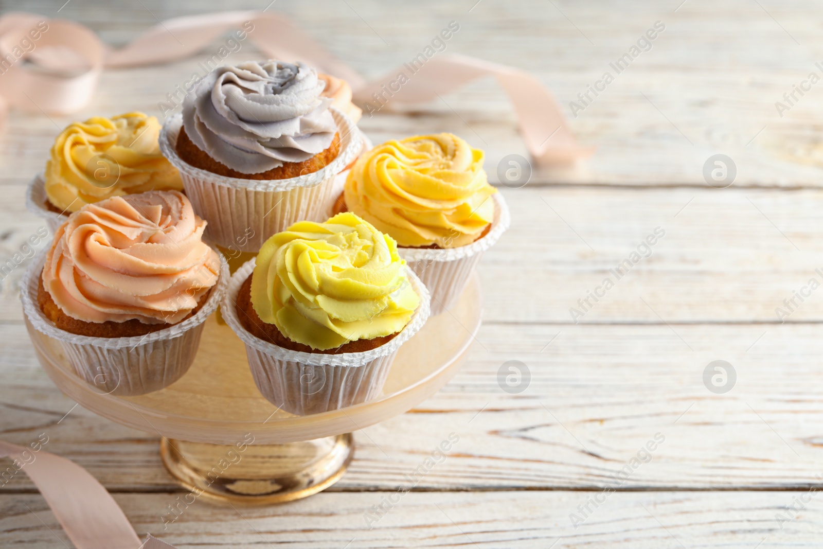 Photo of Stand with tasty cupcakes on white wooden table. Space for text