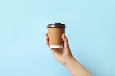 Woman holding takeaway paper coffee cup on light blue background, closeup