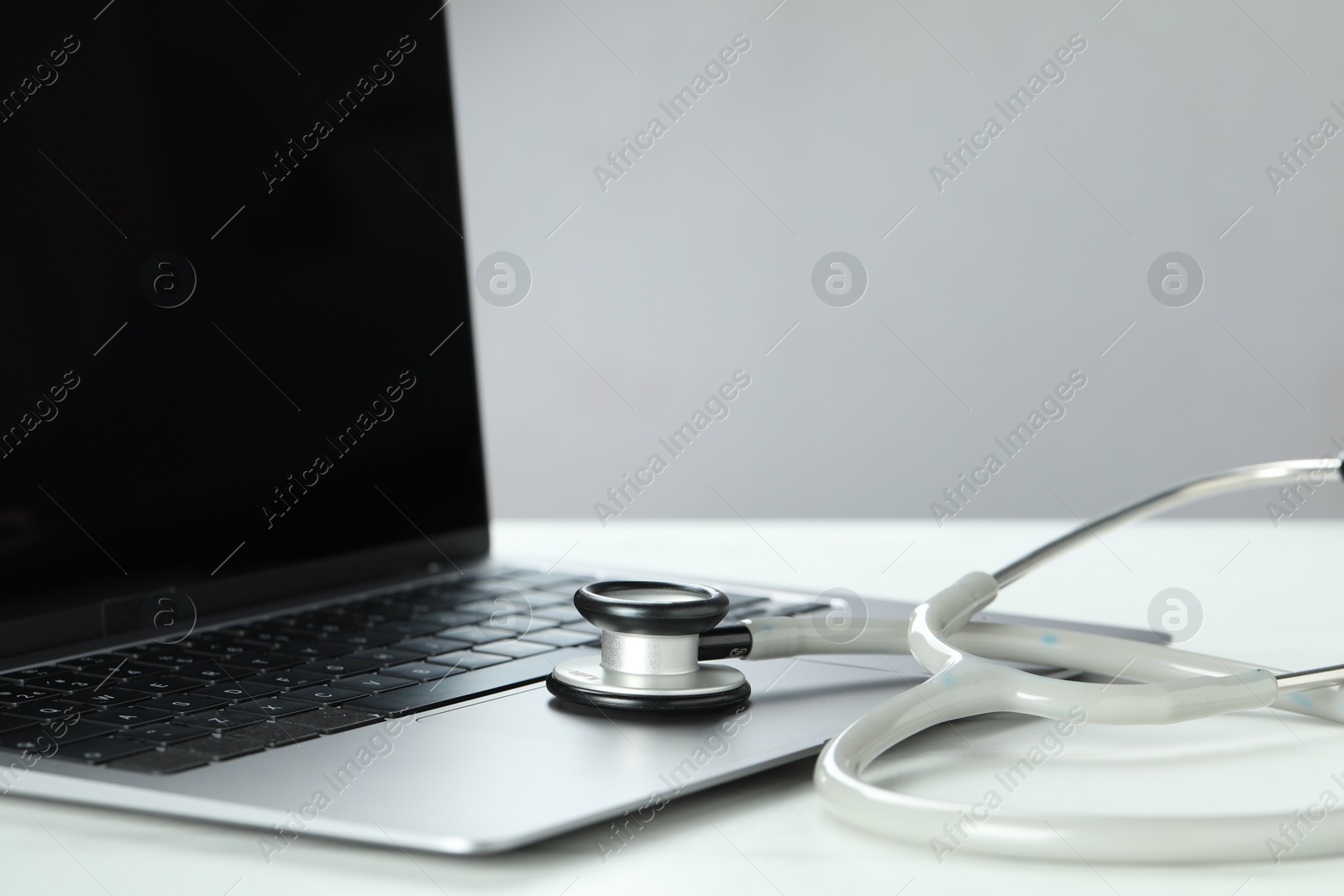 Photo of Modern laptop and stethoscope on white table, closeup. Space for text