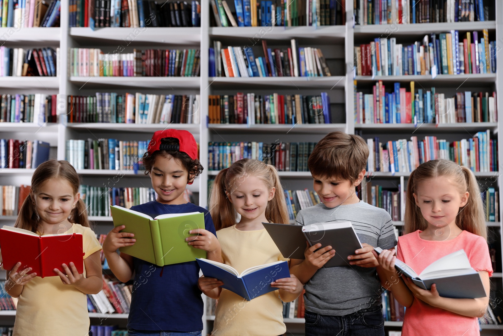 Photo of Group of little children reading books near shelves in library