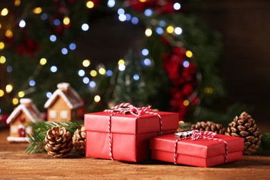 Christmas present. Beautiful gift boxes, cones and fir tree branches on wooden table against blurred festive lights, space for text