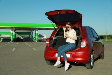 Photo of Beautiful young woman with coffee near car at gas station