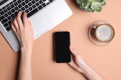 Photo of Woman using smartphone while working with laptop at coral table, top view