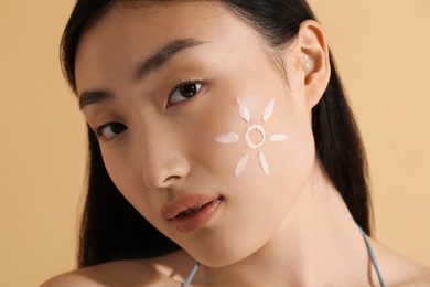 Photo of Beautiful young woman with sun protection cream on her face against beige background, closeup