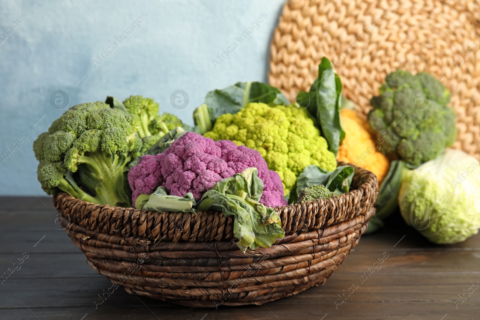 Photo of Wicker basket with different cabbages on wooden table. Healthy food