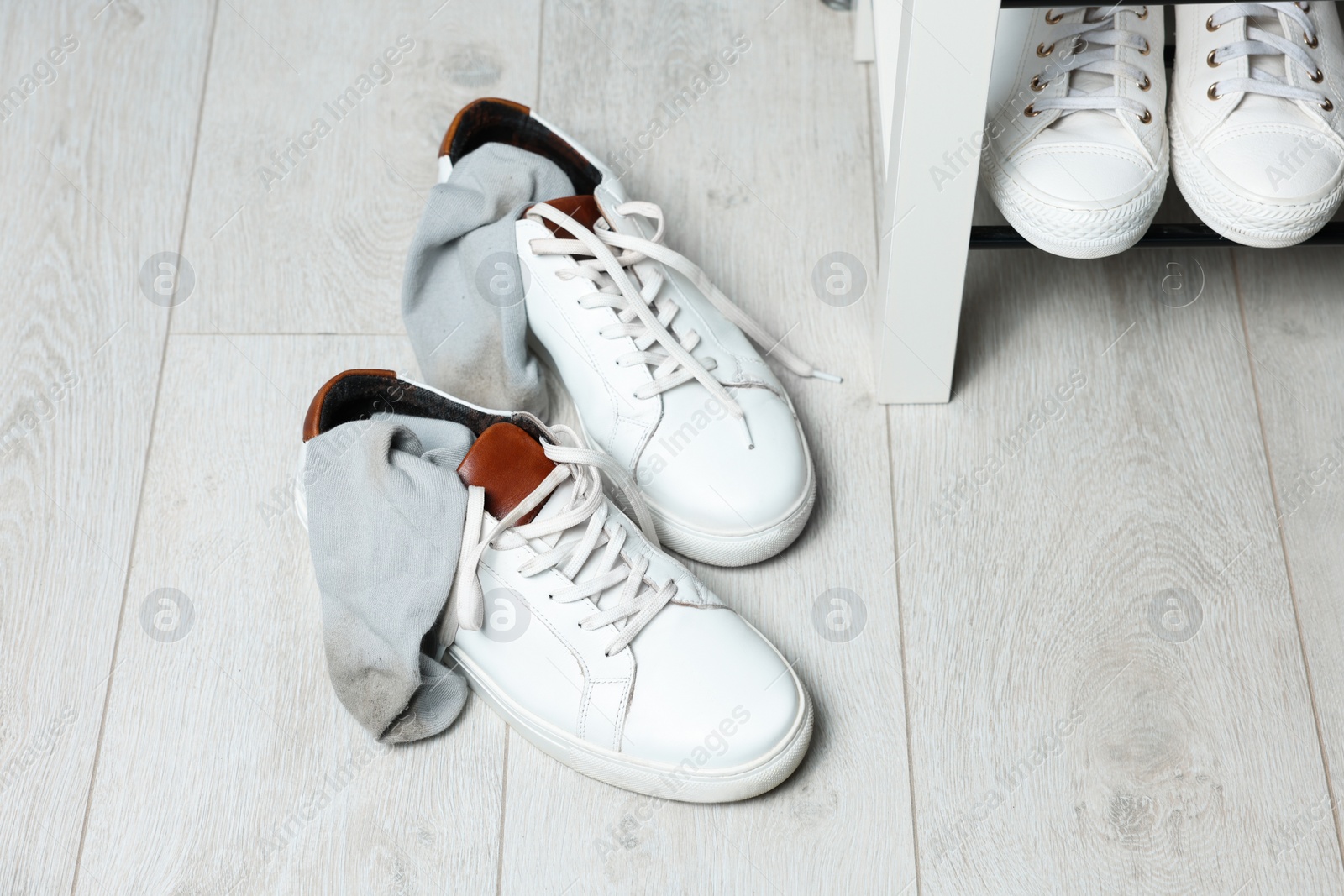 Photo of Sneakers with dirty socks on white wooden floor indoors