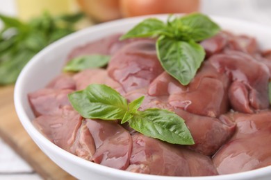 Photo of Bowl with raw chicken liver and basil on table, closeup