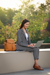 Photo of Beautiful young woman with stylish backpack and laptop on bench in park