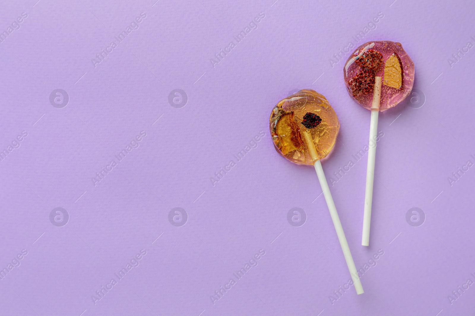 Photo of Sweet colorful lollipops with berries on lilac background, flat lay. Space for text