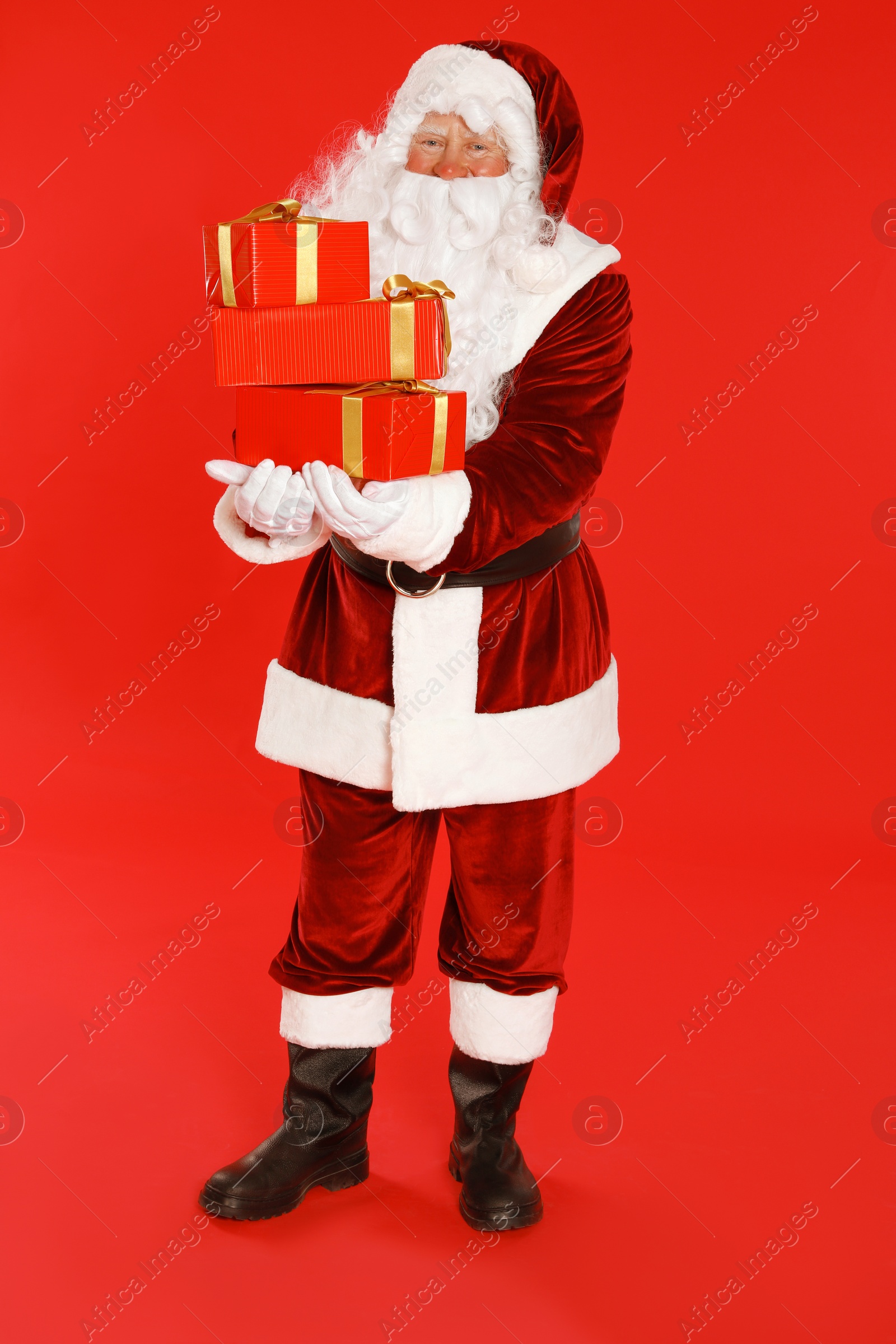 Photo of Authentic Santa Claus with gift boxes on red background
