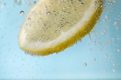 Photo of Juicy lemon slice in soda water against light blue background, closeup