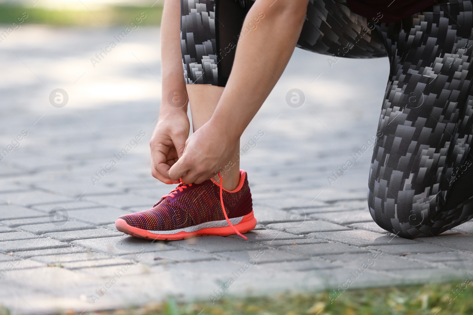 Photo of Young woman tying shoelaces before running in park, focus on legs