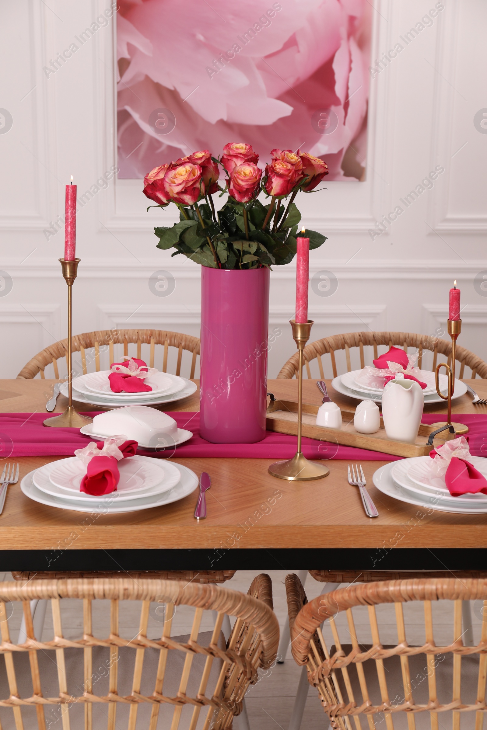 Photo of Color accent table setting. Plates, cutlery, pink napkins and vase with beautiful roses in dining room