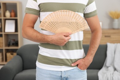 Man with hand fan at home, closeup