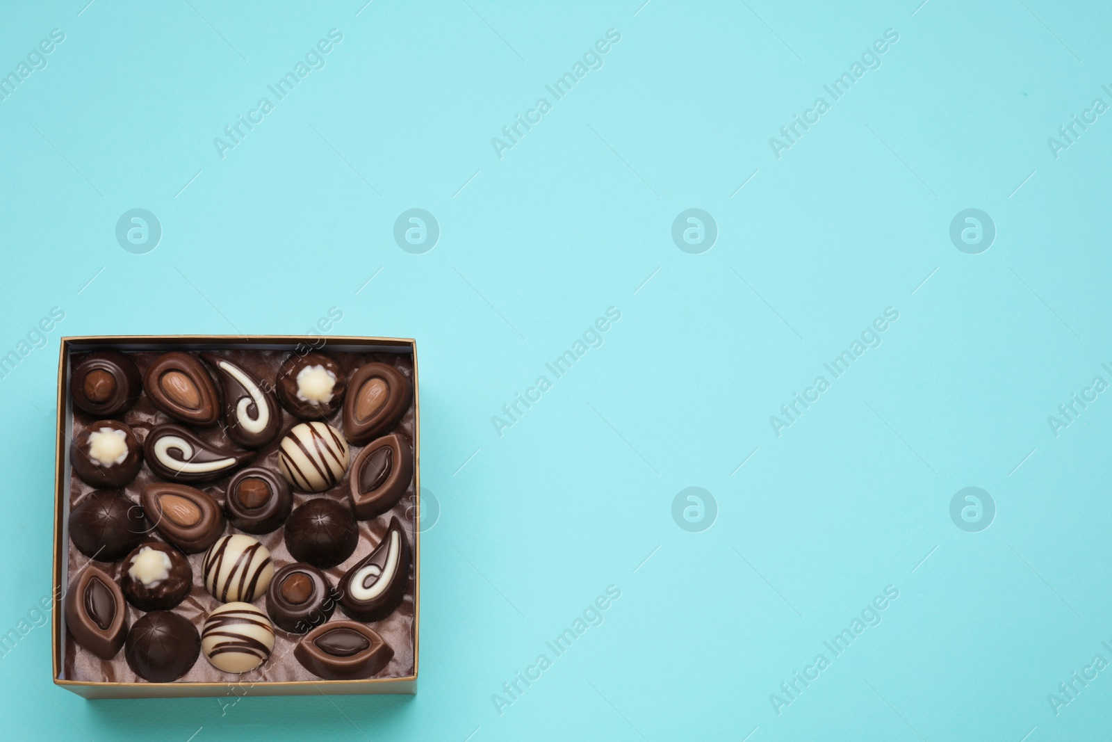 Photo of Box of delicious chocolate candies on light blue background, top view. Space for text