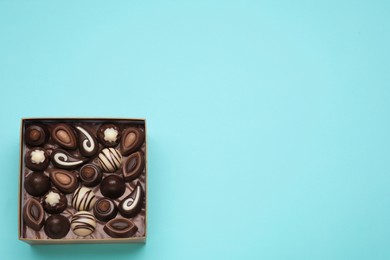 Photo of Box of delicious chocolate candies on light blue background, top view. Space for text
