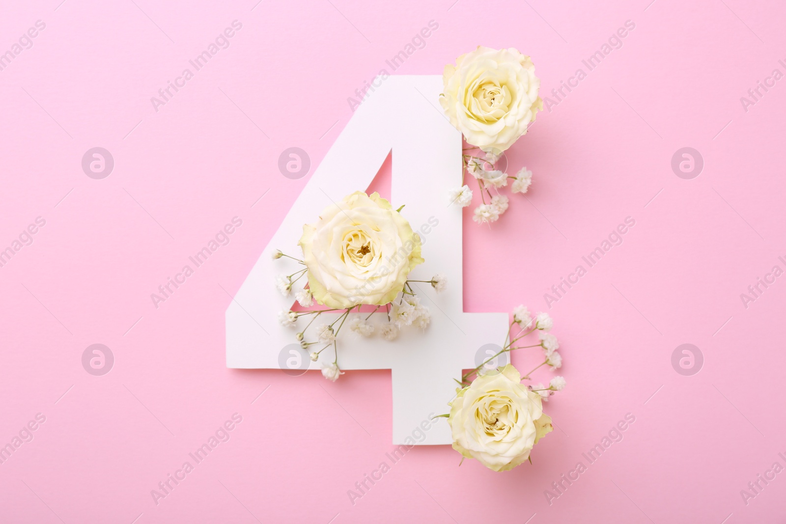 Photo of Paper number 4 and beautiful flowers on pink background, top view