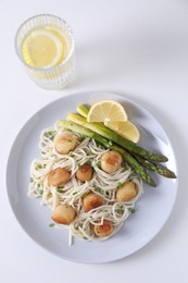 Photo of Delicious scallop pasta with asparagus, green onion and lemon on white table, flat lay