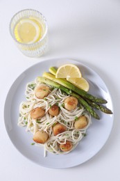 Delicious scallop pasta with asparagus, green onion and lemon on white table, flat lay