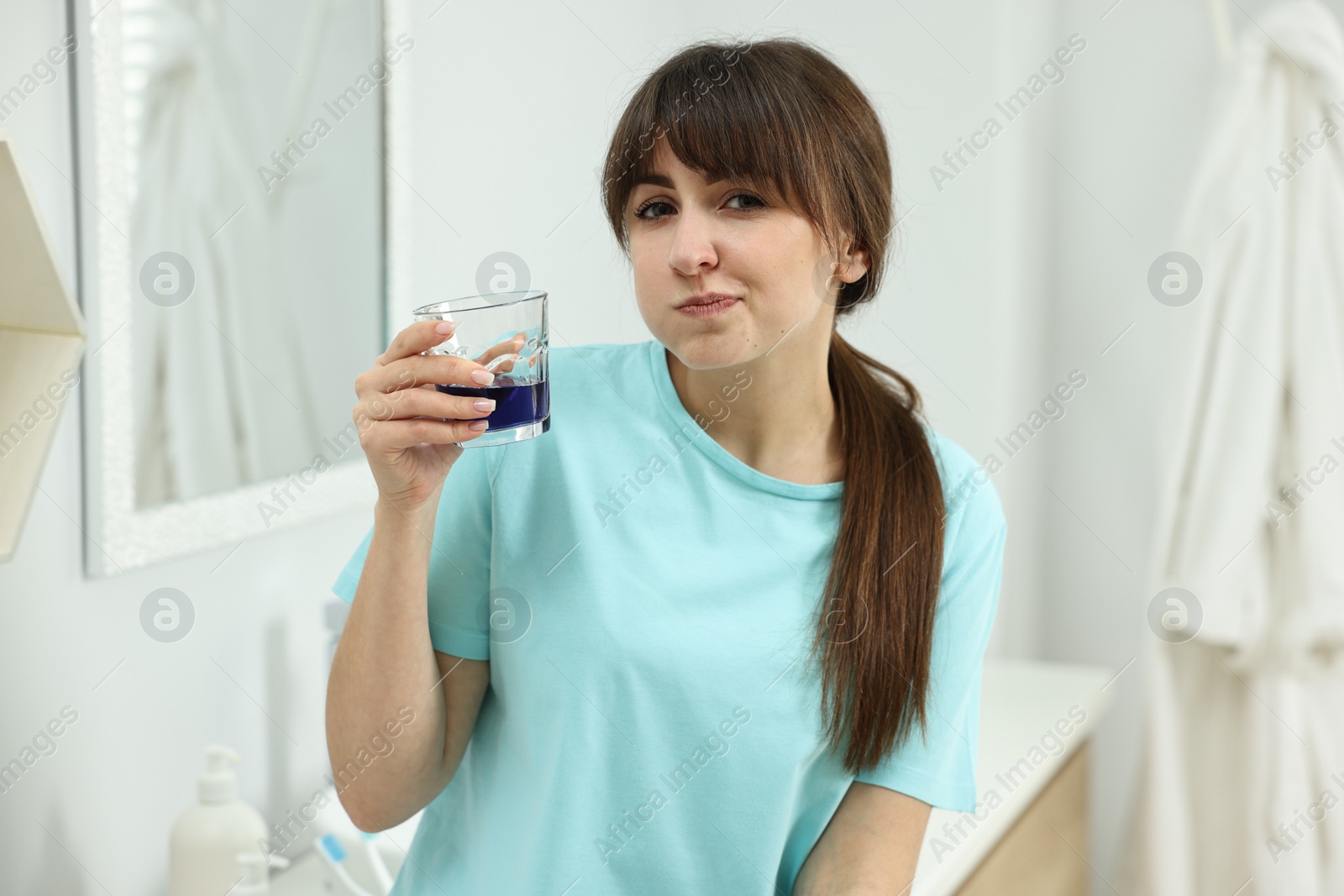 Photo of Young woman using mouthwash in bathroom. Oral hygiene