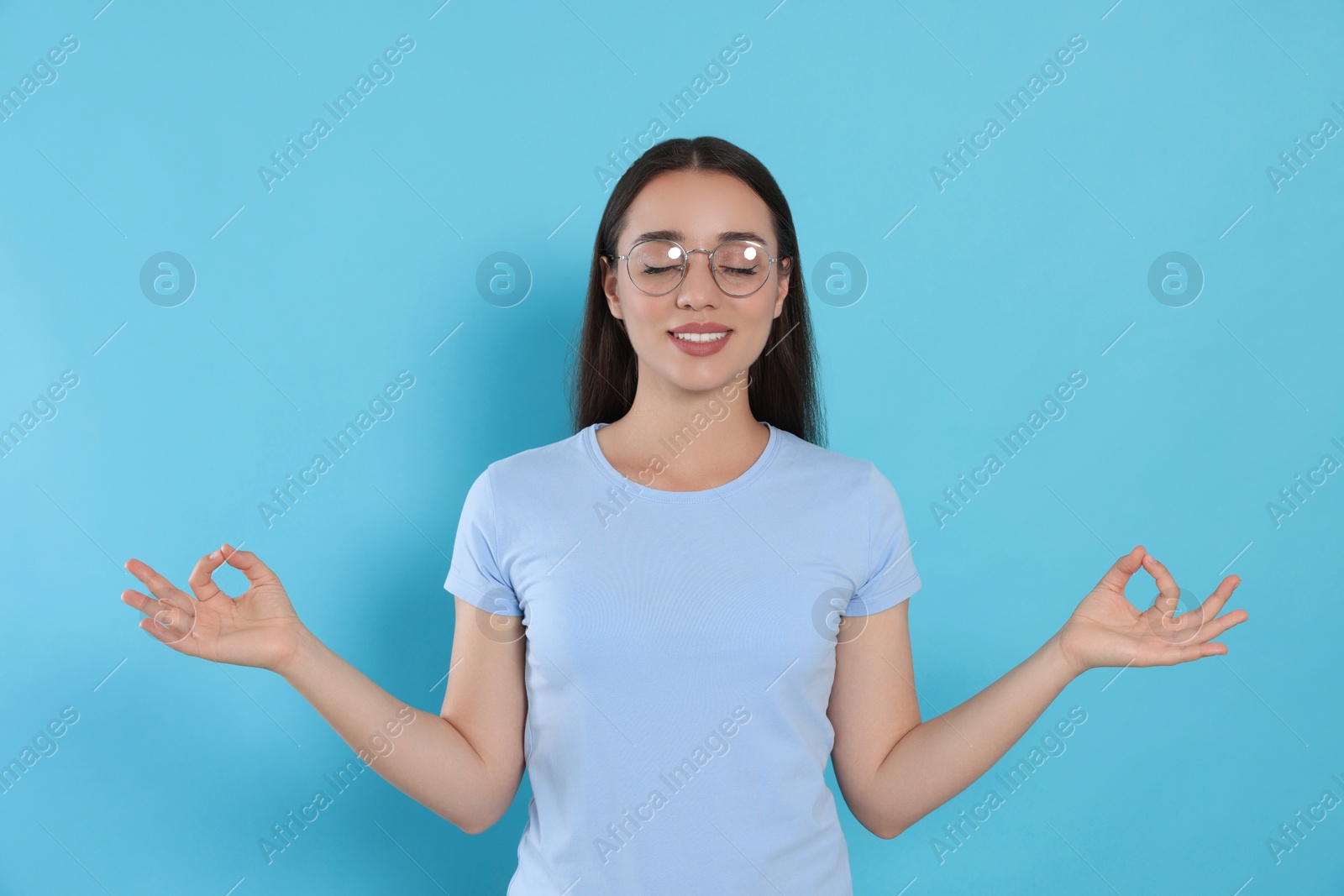 Photo of Find zen. Beautiful young woman meditating on light blue background