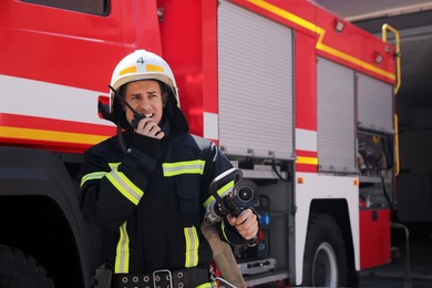 Photo of Firefighter in uniform using portable radio set near fire truck outdoors