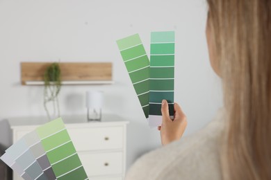 Photo of Woman choosing color for wall in room, focus on hands with paint chips. Interior design