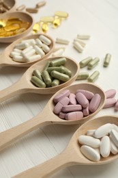 Photo of Different vitamin capsules in spoons on white wooden table, closeup