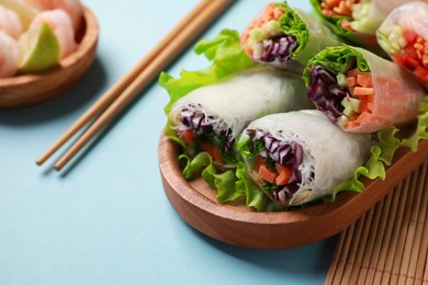 Tasty spring rolls served with lettuce on light blue background, closeup