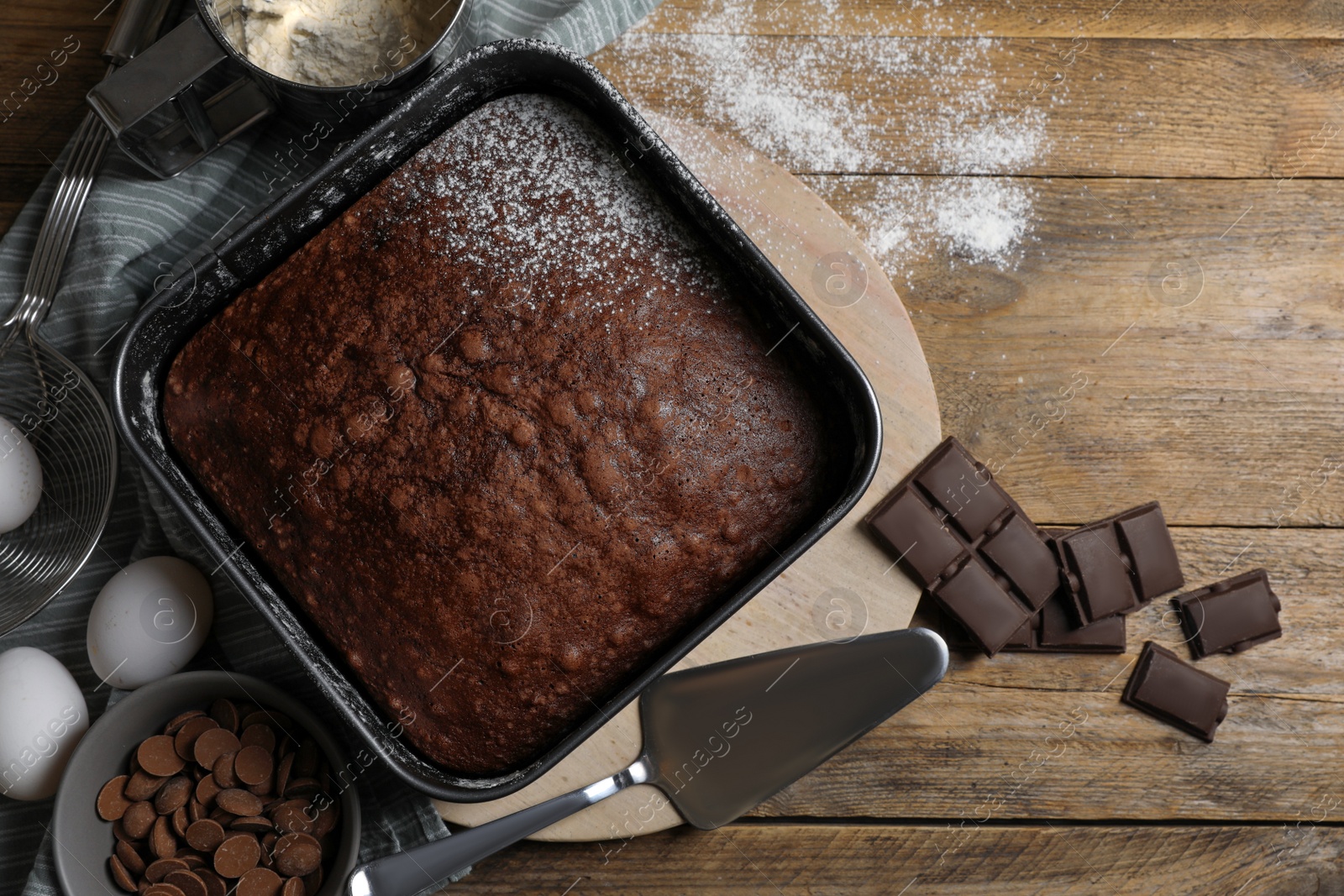 Photo of Homemade chocolate sponge cake and ingredients on wooden table, flat lay