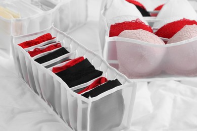 Photo of Organizers with stylish women's underwear on bed, closeup